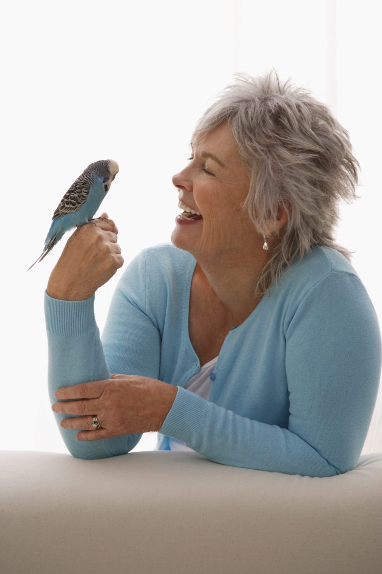 Elderly woman smiling at a blue parakeet perched on her hand, both enjoying a peaceful moment.