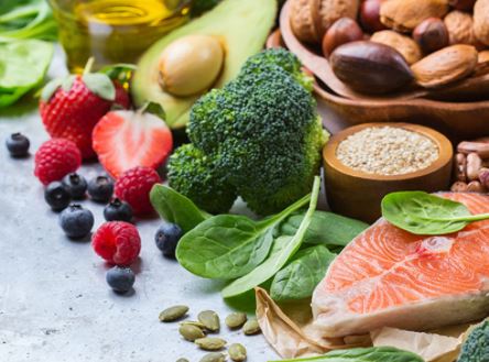 A colorful variety of healthy foods including salmon, vegetables, fruits, nuts, seeds, and olive oil.