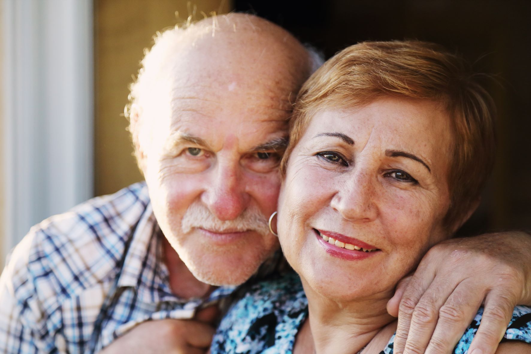 Elderly couple smiling and embracing in close-up, expressing affection and contentment.