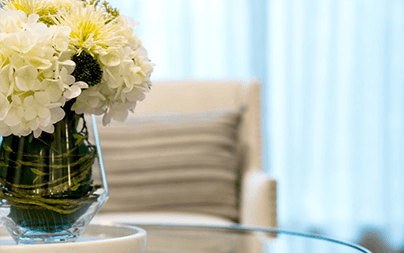 A glass vase with white flowers on a glass table in a modern, softly lit living room.