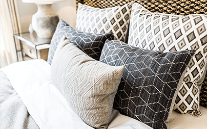 Decorative bed pillows in black and white geometric patterns on a neatly made bed with a bedside lamp.