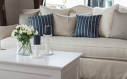 Elegant living room with a beige sofa, striped blue cushions, and white coffee table with flowers.