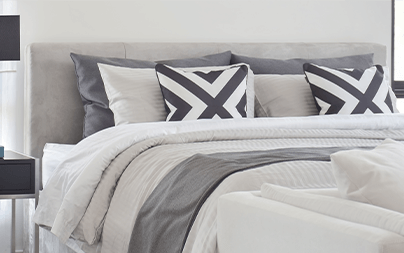 Modern gray bed with geometric throw pillows and crisp white linens in a contemporary bedroom.