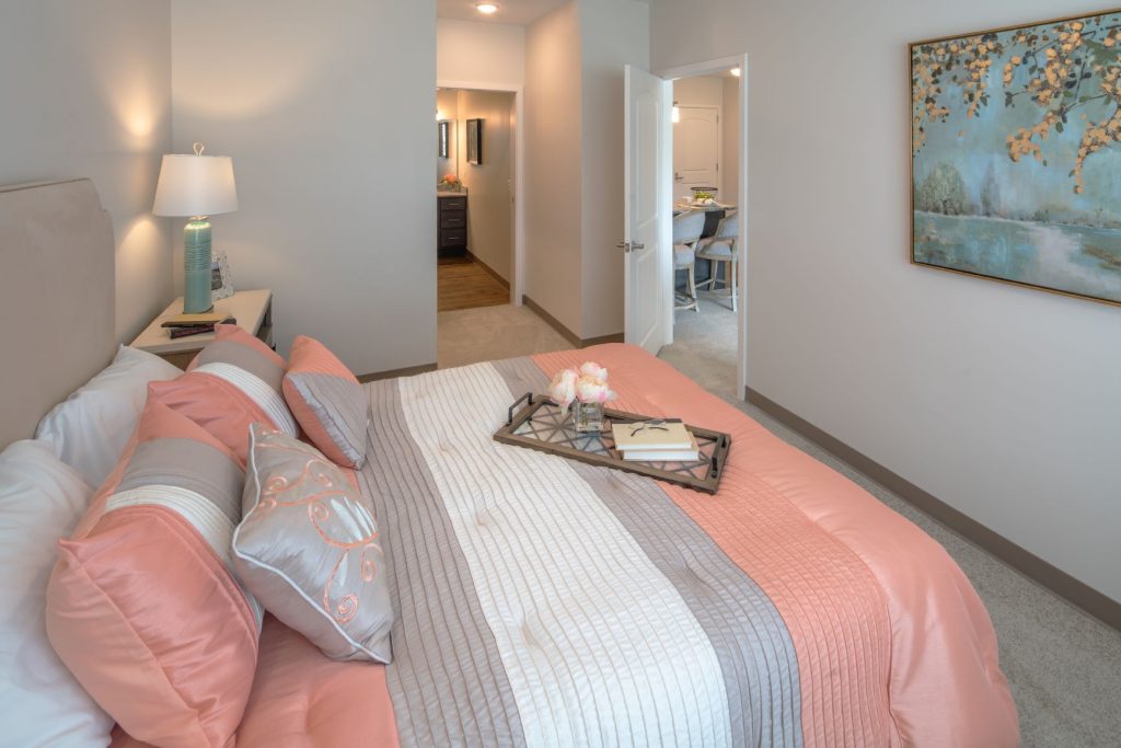 Modern bedroom with pastel decor, tray on bed, and open door to hallway and dining area.