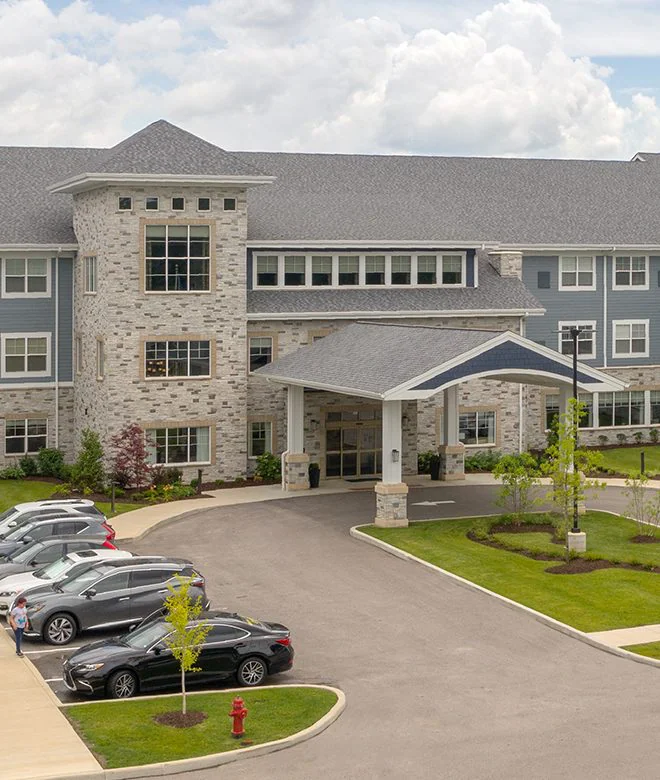 The front entrance of a modern stone and siding building with a covered driveway and parked cars.