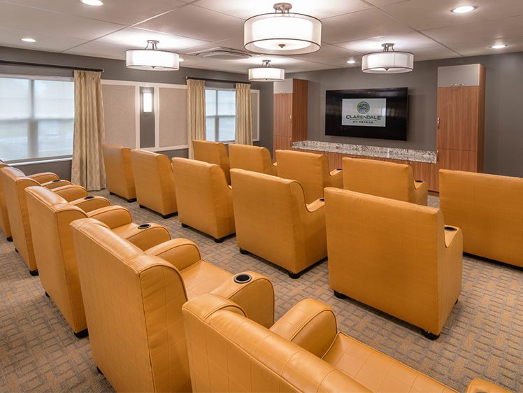 Modern movie theatre room with rows of tan leather seats and a large screen at the front.