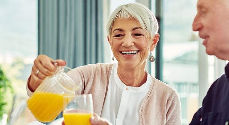 Happy senior woman pours a glass of juice at breakfast