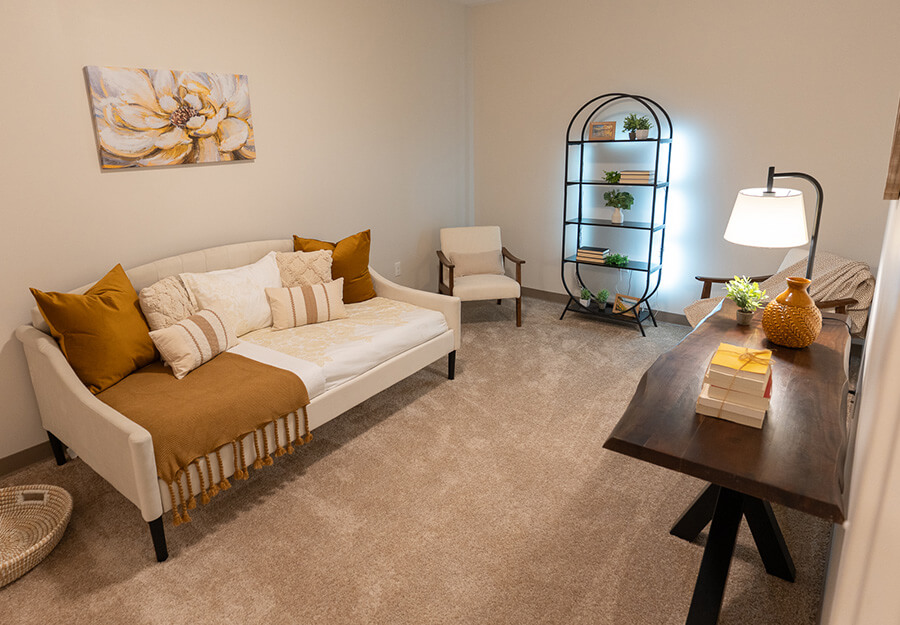 Cozy unit living room with a sofa, chair, bookshelf, and warm lighting.