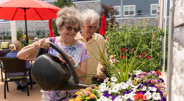 Elderly couple watering flowers in a vibrant garden area at a community unit.