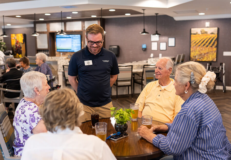 Residents and staff member engaging at a table in a lively community dining area.