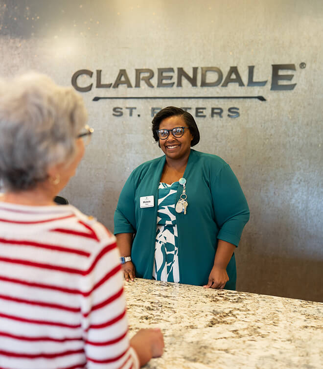 Receptionist greets a woman at the front desk of a living community.