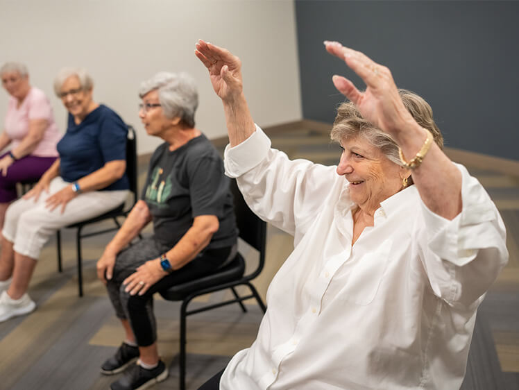 Seniors in a group exercise class, smiling and raising arms.