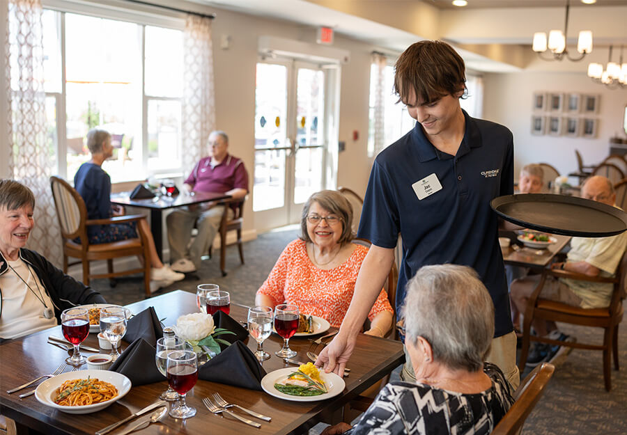 Young man serves senior women dinner at their table